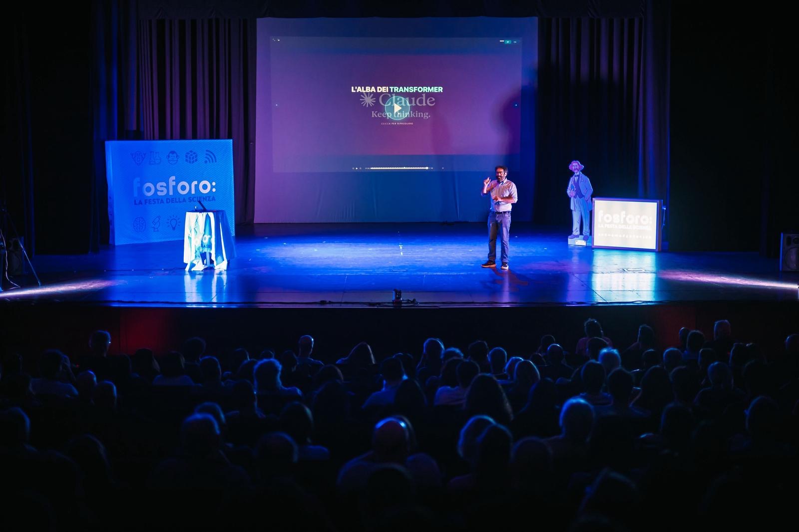Il teatro gremito durante la conferenza-spettacolo, sullo schermo il titolo «L'alba dei Transformer»